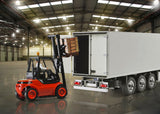Detailed red forklift transporting cargo in a spacious industrial warehouse with bright lighting and a large white trailer.