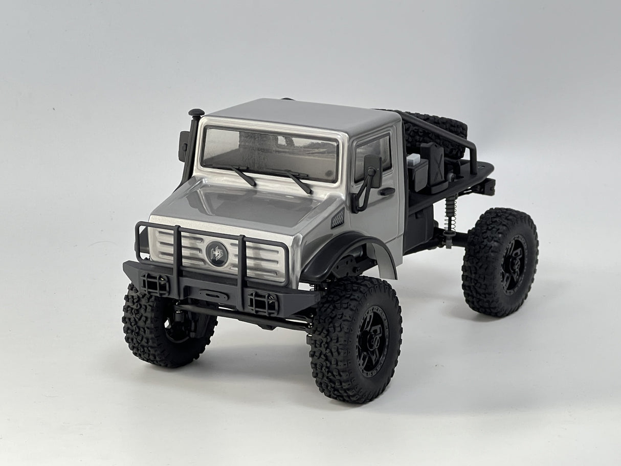 Detailed 1/18 scale remote-controlled silver trail truck with rugged off-road tires and all-terrain capabilities.