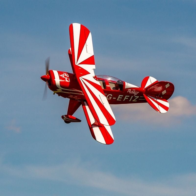 Vibrant red and white Pitts S-2B 60cc ARF RC plane in flight against a blue sky.