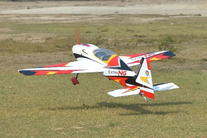 Sleek red and white RC plane, the Phoenix Model Extra Next Gen 50cc Carbon ARF, ready for aerial maneuvers on the grassy field.