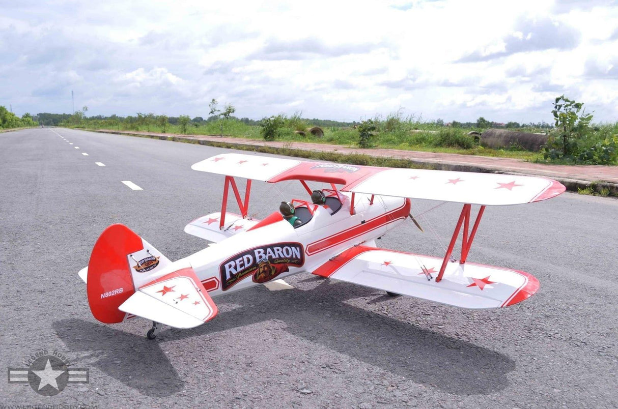 Detailed RC plane model, the Seagull PT-17 Stearman Red Baron 20cc ARF, displayed on a paved road with a scenic rural landscape in the background.