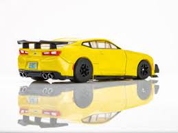 Bright yellow Camaro 1LE slot car with spoiler and racing decals on reflective surface.