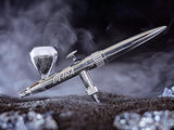 Sleek silver airbrush with chrome accents, surrounded by smoke, resting on a textured surface.