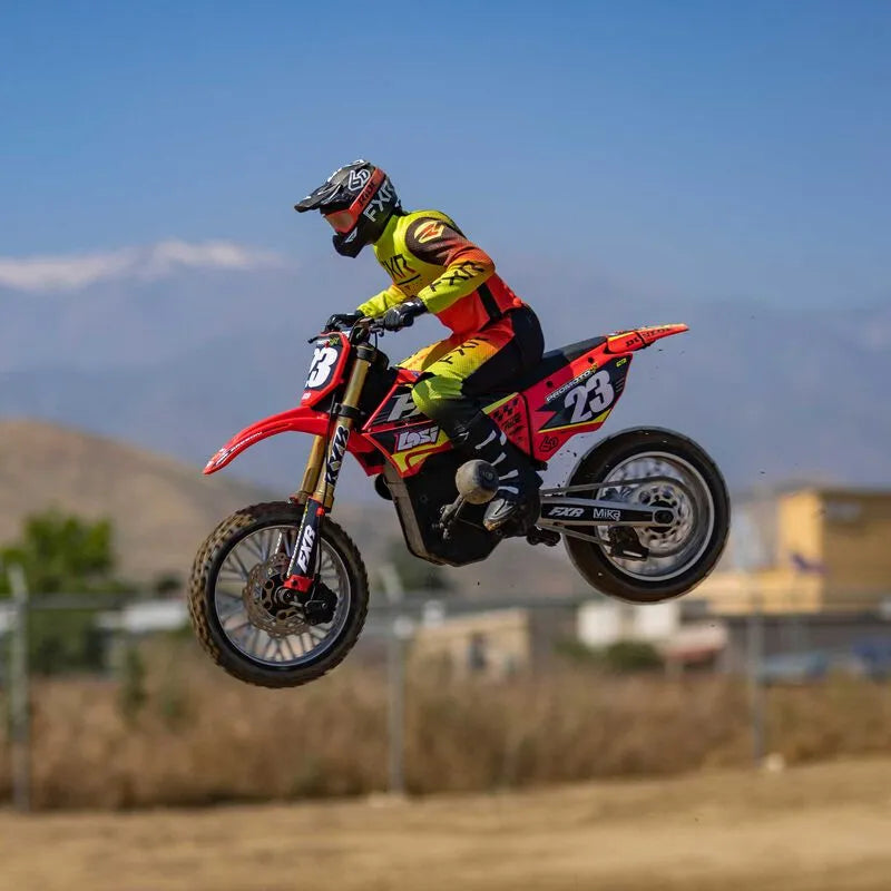Lightweight red and yellow off-road motorcycle in mid-air jump over desert terrain.