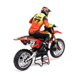 Detailed, realistic 1/4 scale RC motorcycle with rider in bright orange and yellow uniform against a white background.