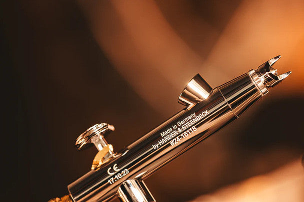 Sleek, dual-nozzle Harder and Steenbeck airbrush in metallic finish, featuring precision control for detailed artwork.