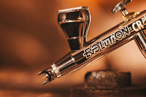 A sleek and precision-engineered Harder and Steenbeck Evolution 2024 CRPlus Solo airbrush with a 0.28mm nozzle, showcased against a warm, rustic background.