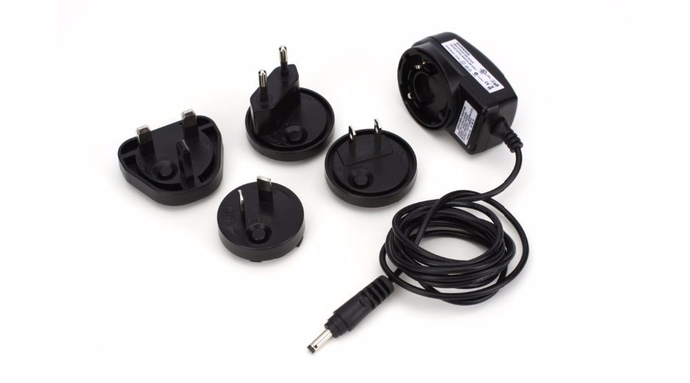 Compact Spektrum International AC power supply with interchangeable plug adapters on a white background.